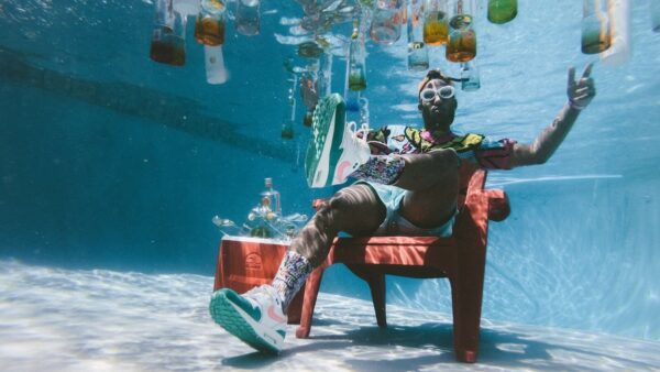 man sitting on chair underwater with floating bottles